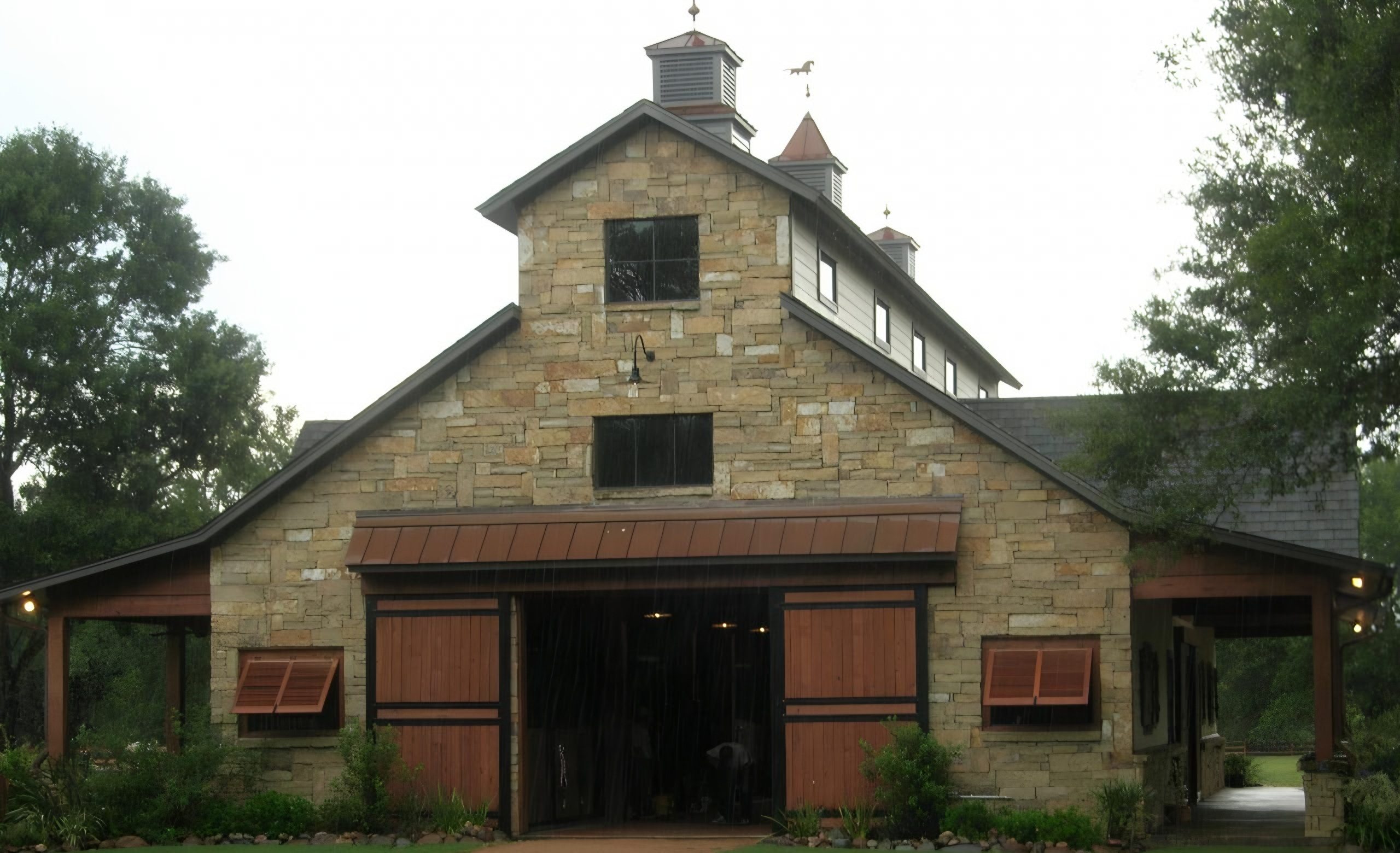 Cypress Stable, a stone horse stable with cupolas and cedar doors, built by Cross Creek Construction